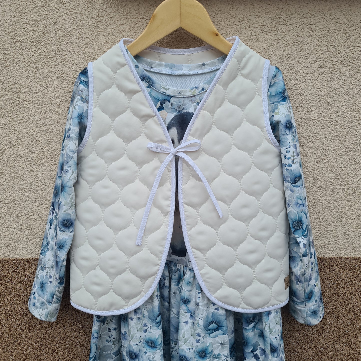 Ručne šitá prešivaná detská vesta na zaväzovanie v krémovej farbe, vyrobená zo 100% polyesteru.